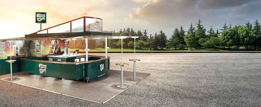 Ein fertig aufgebauter, grüner Ausschankwagen mit integrierter Zapfanlage, Theke und Stehtischen für ein Outdoor-Event.