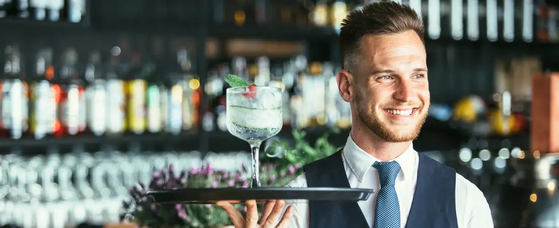 Professioneller Kellner von Timo’s Kellnerservice in Datteln serviert einen Cocktail auf einem Tablett an einer Bar.