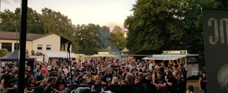 Eine große Menschenmenge auf einem Open-Air-Festival mit Getränkeständen und Essensbuden im Hintergrund.