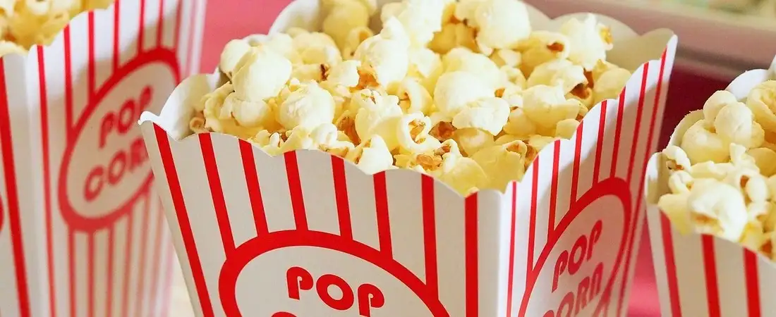Mehrere klassische, rot-weiß gestreifte Popcorn-Tüten, großzügig gefüllt mit frischem Popcorn, stehen bereit für die Gäste eines Events.