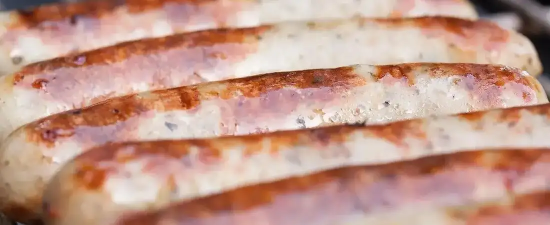 Nahaufnahme von frisch gegrillten Bratwürsten auf dem Grill, zubereitet im mobilen Imbisswagen von Timo’s Kellnerservice.