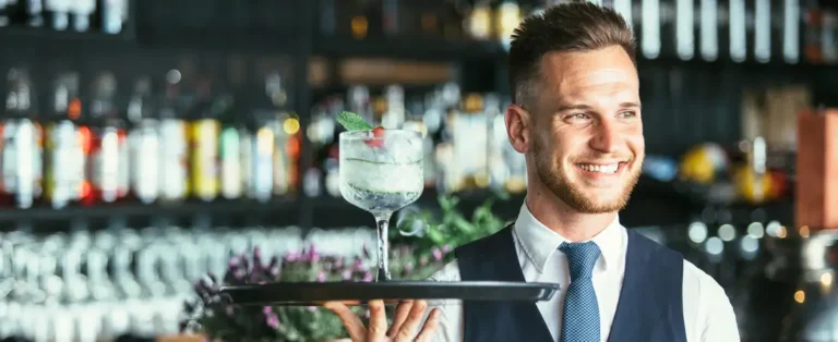 Professioneller Kellner von Timo’s Kellnerservice in Datteln serviert einen Cocktail auf einem Tablett an einer Bar.
